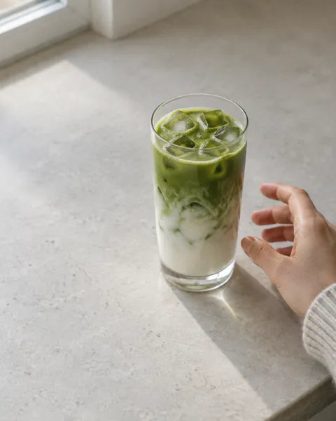 Vaso de matcha con leche y hielo sobre una encimera clara.