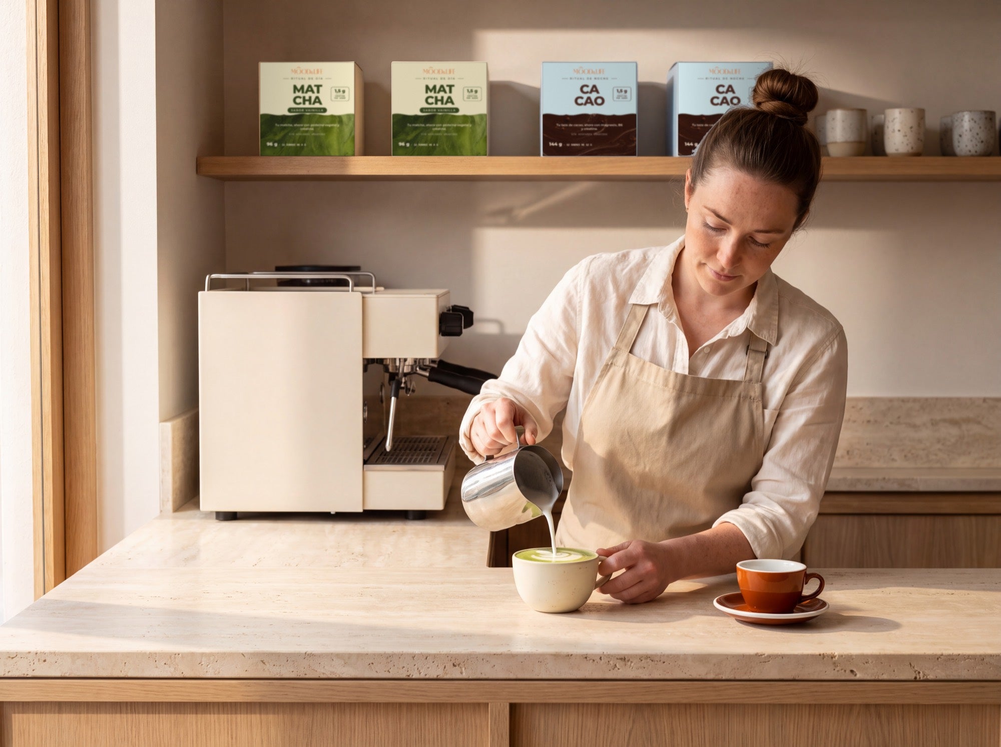 Barra de cafetería con una barista preparando un matcha y cajas de Mood & Life en la balda.