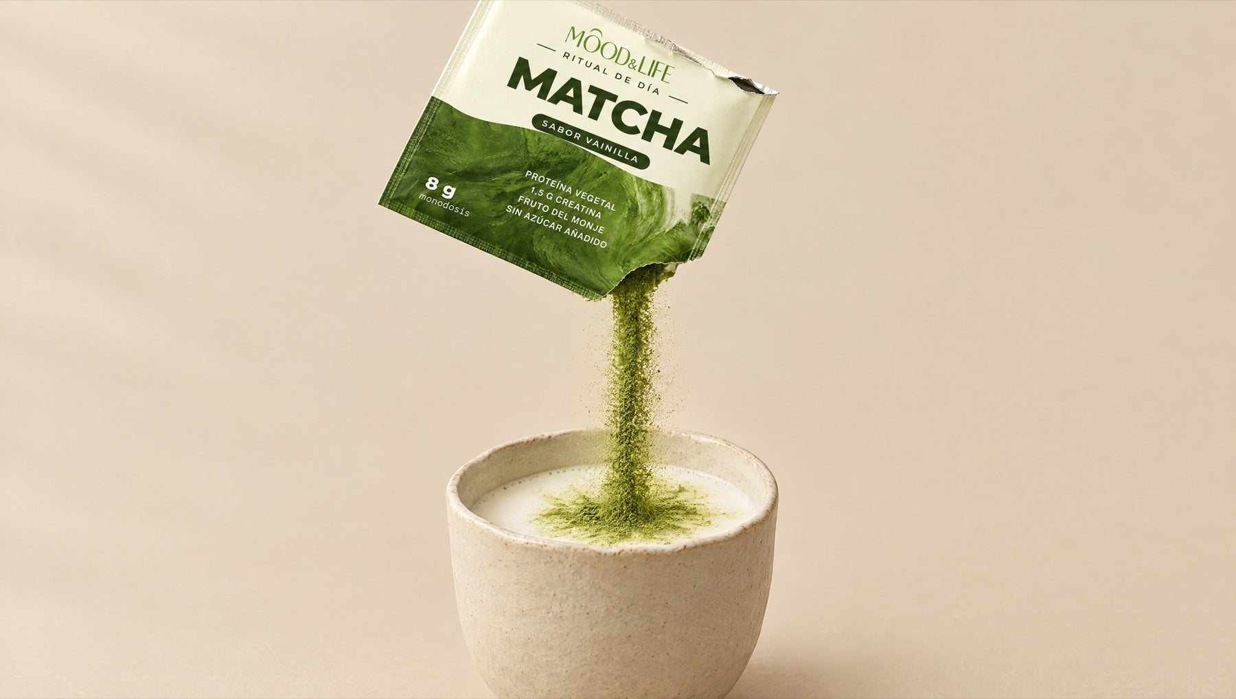 Polvo de matcha cayendo de un sobre a una taza con leche.