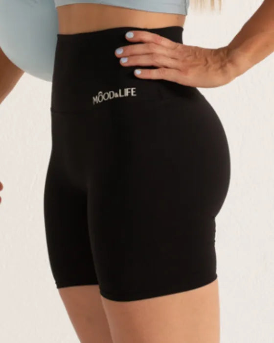 Short negro de cintura alta con el logo en la cinturilla, visto de lado; arriba asoma un top azul claro.
