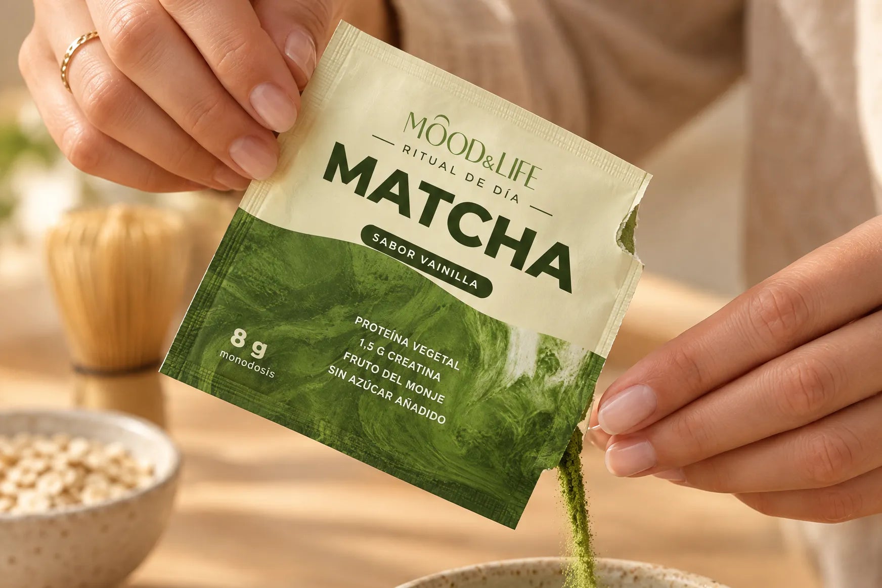 Unas manos abren un sobre de Matcha Ritual y dejan caer el polvo verde en un cuenco de gres, sobre una mesa de madera con luz de mañana.